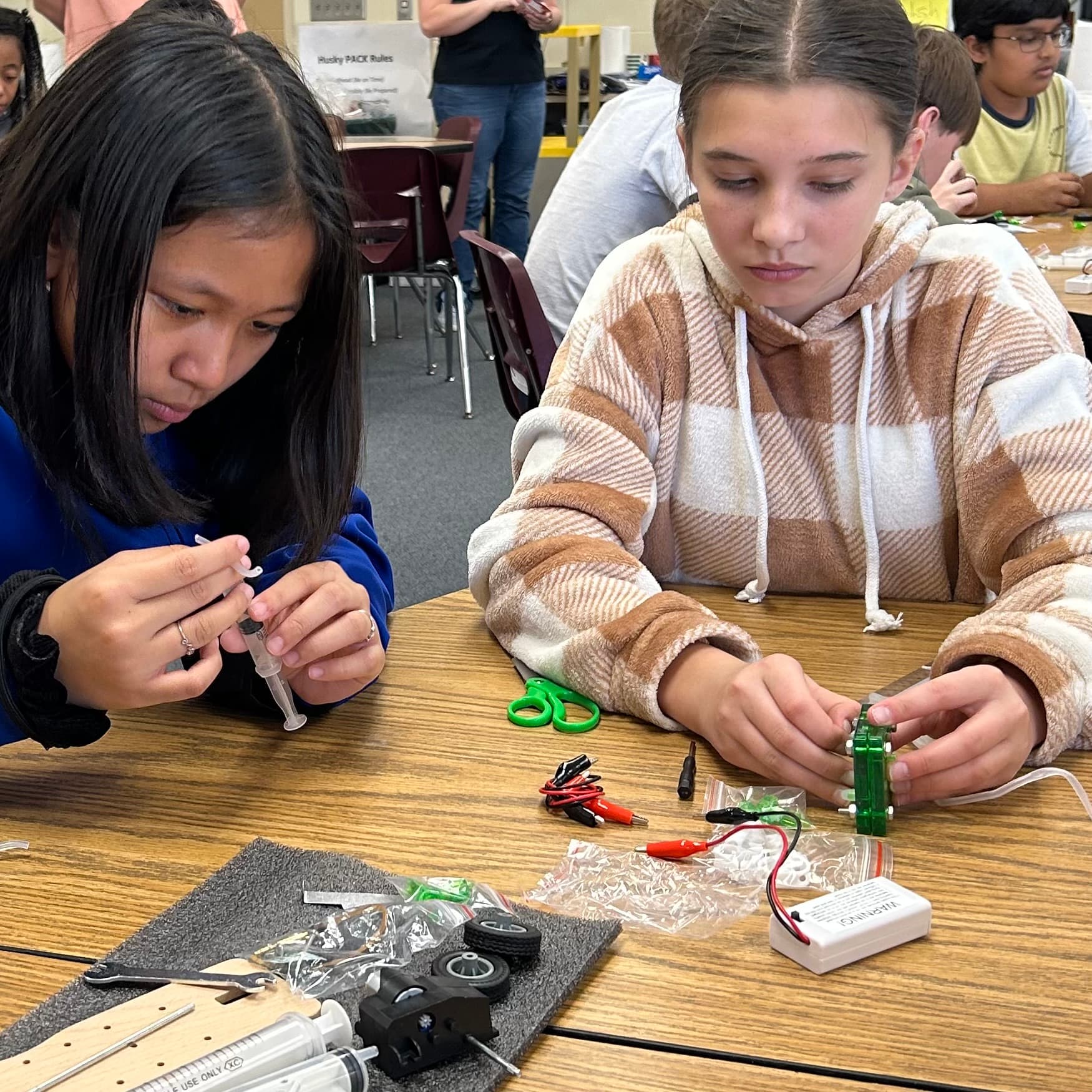 Two girls at a table focused on putting together pieces to their project